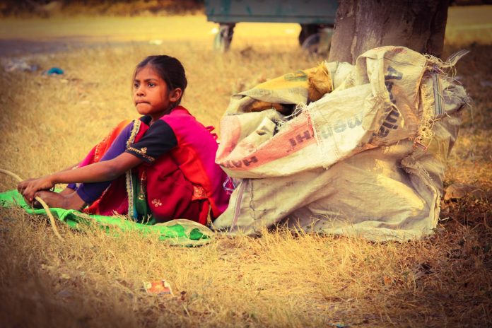 A poor girl sits with sack of waste, In India