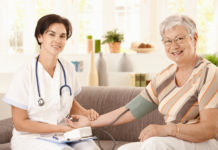 Nurse measuring blood pressure of senior woman at home. Looking at camera, smiling